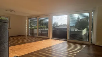 Helles Wohnzimmer mit Holzboden, Kaminofen und Zugang zu einem Balkon oder einer Terrasse.