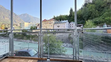 Balkon mit Blick auf den Fluss, umgeben von Bergen und städtischer Bebauung, mit Holzboden.