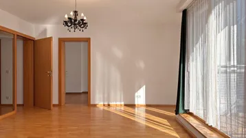 Helles Wohnzimmer mit Parkettboden, großem Fenster und elegantem Kronleuchter, durchflutet von Sonnenlicht.