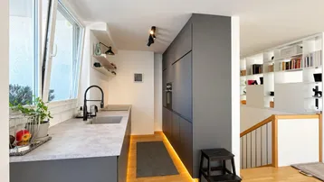 Moderne Küche mit grauen Schränken, integrierten Geräten und Holzboden, offen zum Wohnbereich.