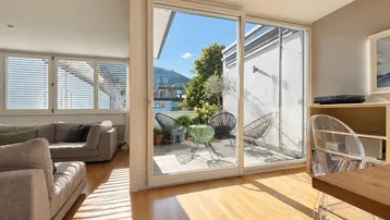 Helles Wohnzimmer mit Holzboden, großen Schiebetüren und Zugang zu einer möblierten Terrasse mit Bergblick.