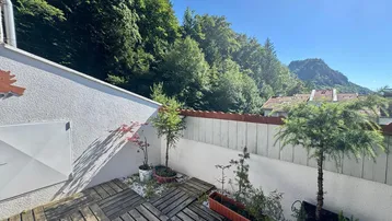 Sonnige Terrasse mit Holzboden, Topfpflanzen und weitem Blick auf grüne Berge.