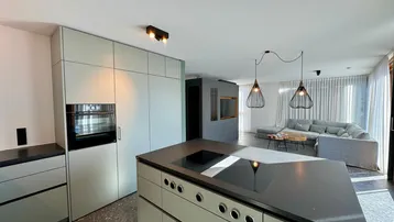 Moderne offene Küche mit Kochinsel und integriertem Backofen, die in einen hellen Wohnbereich übergeht.