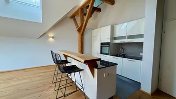 Moderne Küche mit weißer Einbauküche, Frühstücksbar, Holzbalken und Dachfenstern in einem Dachgeschoss.