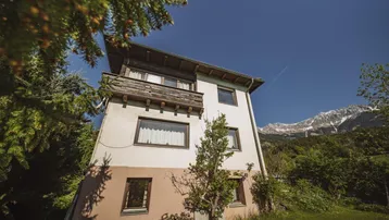 Hausfassade mit Balkon und Blick auf die umliegenden Berge und grüne Landschaft.