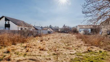 Sonniges Grundstück mit trockenem Gras und umliegenden Häusern, ideal für Neubau.