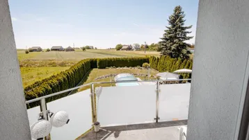 Balkon mit weitem Blick über grüne Felder und einen Garten mit Pool.