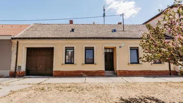 Einfamilienhaus mit beiger Fassade, braunem Garagentor und Ziegeldach unter blauem Himmel.