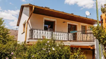 Fassade eines Hauses mit Balkon und schmiedeeisernem Geländer unter blauem Himmel.