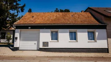 Ansicht der Hausfassade mit weißer Garage, Fenstern und Ziegeldach unter blauem Himmel.