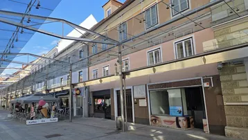 Fassade eines Gebäudes an einer belebten Straße mit Geschäften und einem Café im Erdgeschoss.
