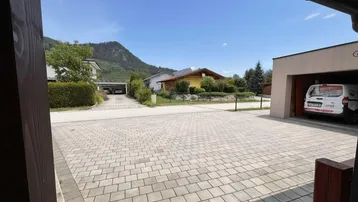 Gepflasterte Einfahrt mit Blick auf die umliegende Wohnsiedlung und bewaldete Berge im Hintergrund.