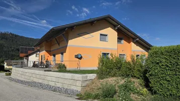 Modernes Einfamilienhaus mit orangefarbener Fassade und gepflegter Außenanlage unter blauem Himmel.