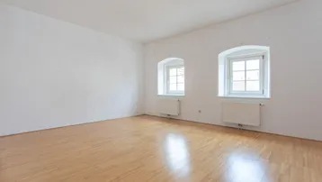 Helles, leeres Zimmer mit Parkettboden und zwei Fenstern, bereit zur individuellen Gestaltung.