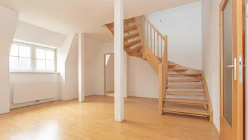 Helles Dachgeschosszimmer mit Holztreppe, Parkettboden und schrägen Wänden, ideal als Wohnbereich.