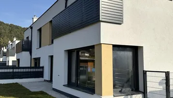 Moderne Reihenhäuser mit weißer Fassade, dunklen Akzenten und kleinem Vorgarten.