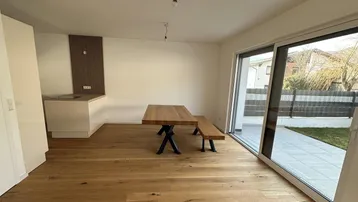 Heller offener Wohn-Essbereich mit Holzboden, moderner Küchenzeile und Zugang zur Terrasse.