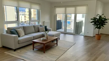 Helles Wohnzimmer mit modernem Sofa, Holzboden und Zugang zu einem Balkon.