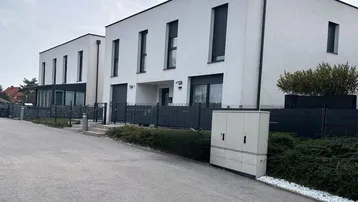 Moderne Reihenhäuser mit weißer Fassade und großen Fenstern an einer ruhigen Straße.