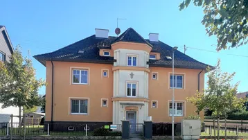 Vorderansicht eines Mehrfamilienhauses mit oranger Fassade, dunklem Dach und einem markanten Erker.