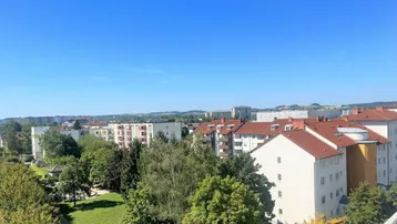 Weitläufiger Blick über die Stadt mit viel Grün und Wohngebäuden unter blauem Himmel.
