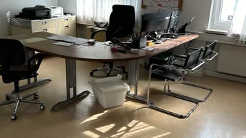 Geräumiges Büro mit mehreren Arbeitsplätzen, Schreibtischen und Fenstern, die viel Tageslicht hereinlassen.