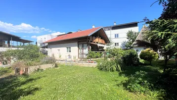 Großzügiger Gartenbereich mit Rasenfläche und Blick auf das Wohnhaus unter blauem Himmel.