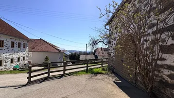 Ländliche Straße führt an historischen Gebäuden vorbei mit weitem Blick in die hügelige Landschaft.