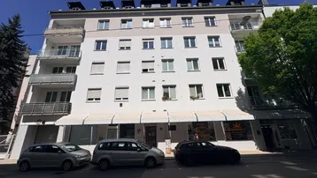 Mehrstöckiges Wohngebäude mit weißer Fassade, Balkonen und Geschäften im Erdgeschoss.