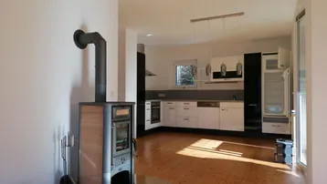 Heller offener Wohnbereich mit modernem Holzofen und integrierter Küche, ideal für gemütliche Abende.