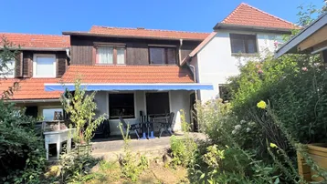 Geräumige Terrasse mit Markise und Gartenmöbeln, umgeben von üppigem Grün hinter dem Haus.