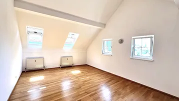 Helles Dachzimmer mit Holzboden, Dachschrägen und zwei Dachfenstern für viel Tageslicht.