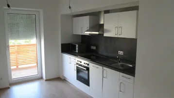 Moderne Küchenzeile mit weißen Schränken, dunkler Arbeitsplatte und Zugang zu einem Balkon.