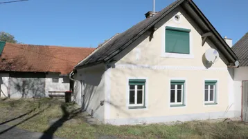 Traditionelles Landhaus mit gelber Fassade, grünen Fensterläden und Satteldach in ländlicher Umgebung.