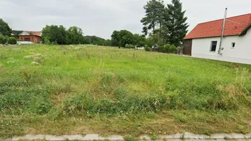 Weitläufiges grünes Grundstück mit einem Haus im Hintergrund, umgeben von Bäumen und ländlicher Natur.