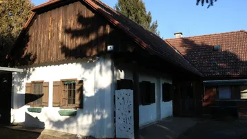 Traditionelles Landhaus mit weißer Fassade, Holzverkleidung und braunen Fensterläden unter blauem Himmel.