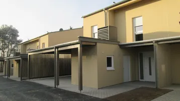 Moderne Reihenhäuser mit beigefarbener Fassade und integrierten Carports in einer Wohnsiedlung.