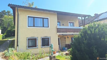 Gelbe Fassade eines Einfamilienhauses mit Balkon und kleinen Fenstern unter blauem Himmel.