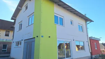 Modernes Gebäude mit weißer und lindgrüner Fassade, großen Fenstern und einem Eingangsbereich.