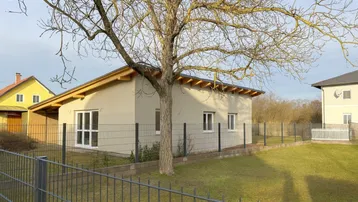 Ansicht des im Bau befindlichen Einfamilienhauses mit Gartenbereich, Zaun und umliegender Bebauung.