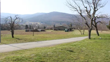 Weitläufige ländliche Landschaft mit Feldern, Bäumen und Bergen im Hintergrund unter blauem Himmel.