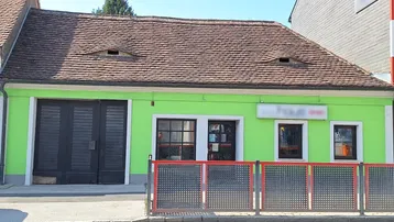 Grünes Gebäude mit braunem Ziegeldach und großen schwarzen Garagentoren an der Straßenseite.