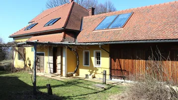Gelbes Landhaus mit rotem Ziegeldach und Solarpaneelen auf dem Dach.