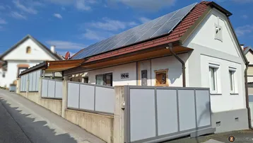 Einfamilienhaus mit Ziegeldach, Photovoltaikanlage und moderner Einfriedung entlang einer Auffahrt.