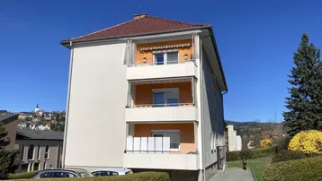 Mehrfamilienhaus mit mehreren Balkonen und Blick auf die umliegende Hügellandschaft.