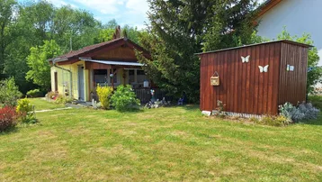 Gepflegter Gartenbereich mit einem kleinen Haus, einem Holzschuppen und viel Grün unter blauem Himmel.