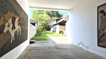 Überdachter Durchgang mit Mosaikbildern führt zu einem ländlichen Hofbereich mit alten Gebäuden.