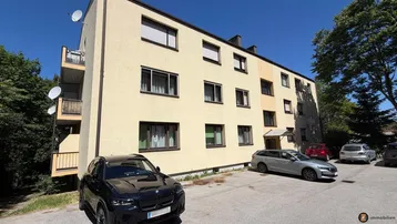 Mehrstöckiges Apartmentgebäude mit beiger Fassade und Parkplätzen im Freien unter blauem Himmel.