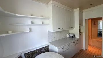 Küchenbereich mit weißen Schränken, offenen Regalen und einer eingebauten Sitzbank mit Tisch.