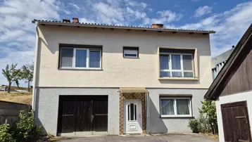 Einfamilienhaus mit beiger Fassade, Doppelgarage und weißer Eingangstür unter blauem Himmel.